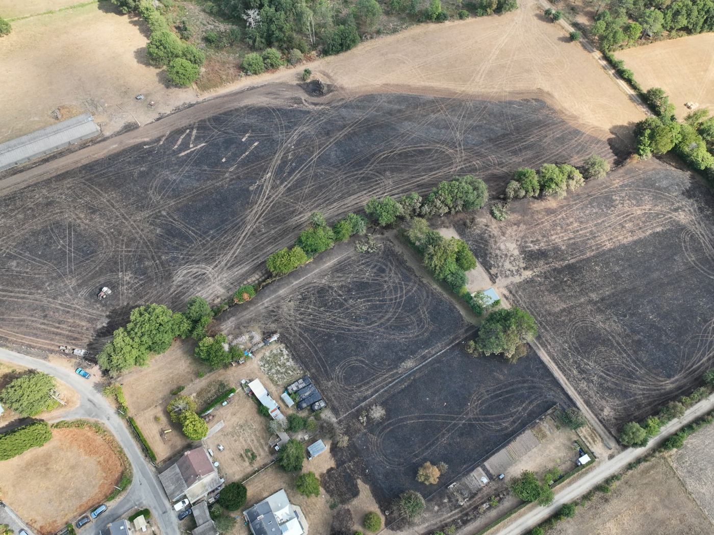 Second angle aérien par drone de la parcelle incendiée dans le Morbihan, montrant la zone brûlée stoppée à quelques mètres des jardins et dépendances des habitations
