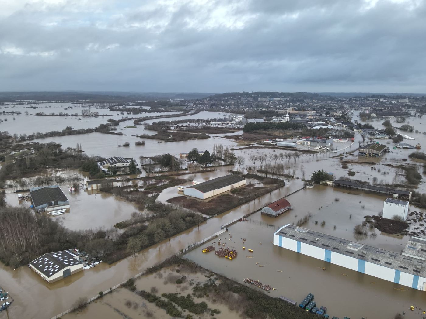 Vue aérienne panoramique par drone des prairies, champs et terre-pleins industriels inondés dans le secteur de Redon en Ille-et-Vilaine, la ville à l'horizon